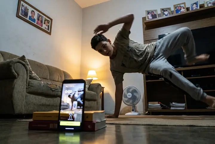 A street dancer on a Rio plaza, a propped phone running the app. AI-generated scene · real app screen